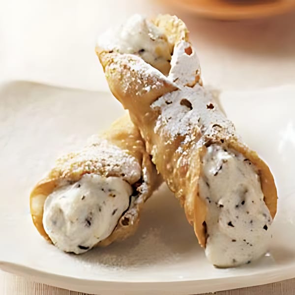 Two cannoli filled with creamy white filling and chocolate chips, dusted with powdered sugar.