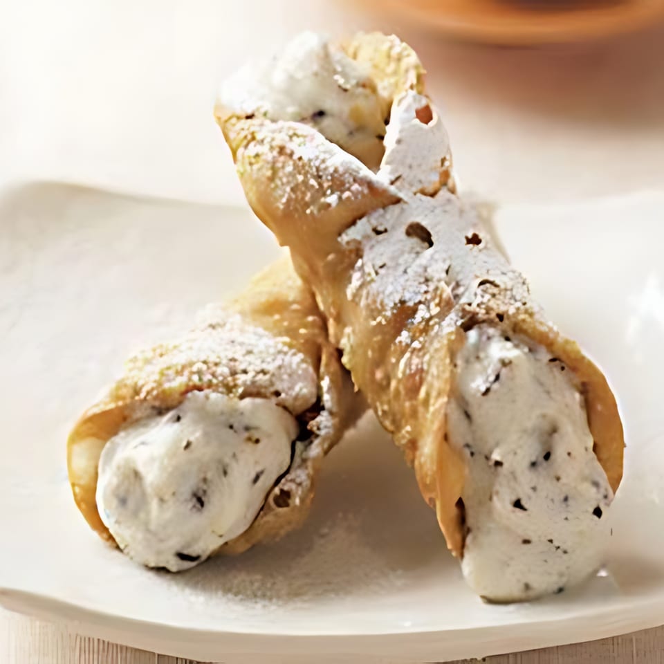 Two cannoli filled with creamy white filling and chocolate chips, dusted with powdered sugar.